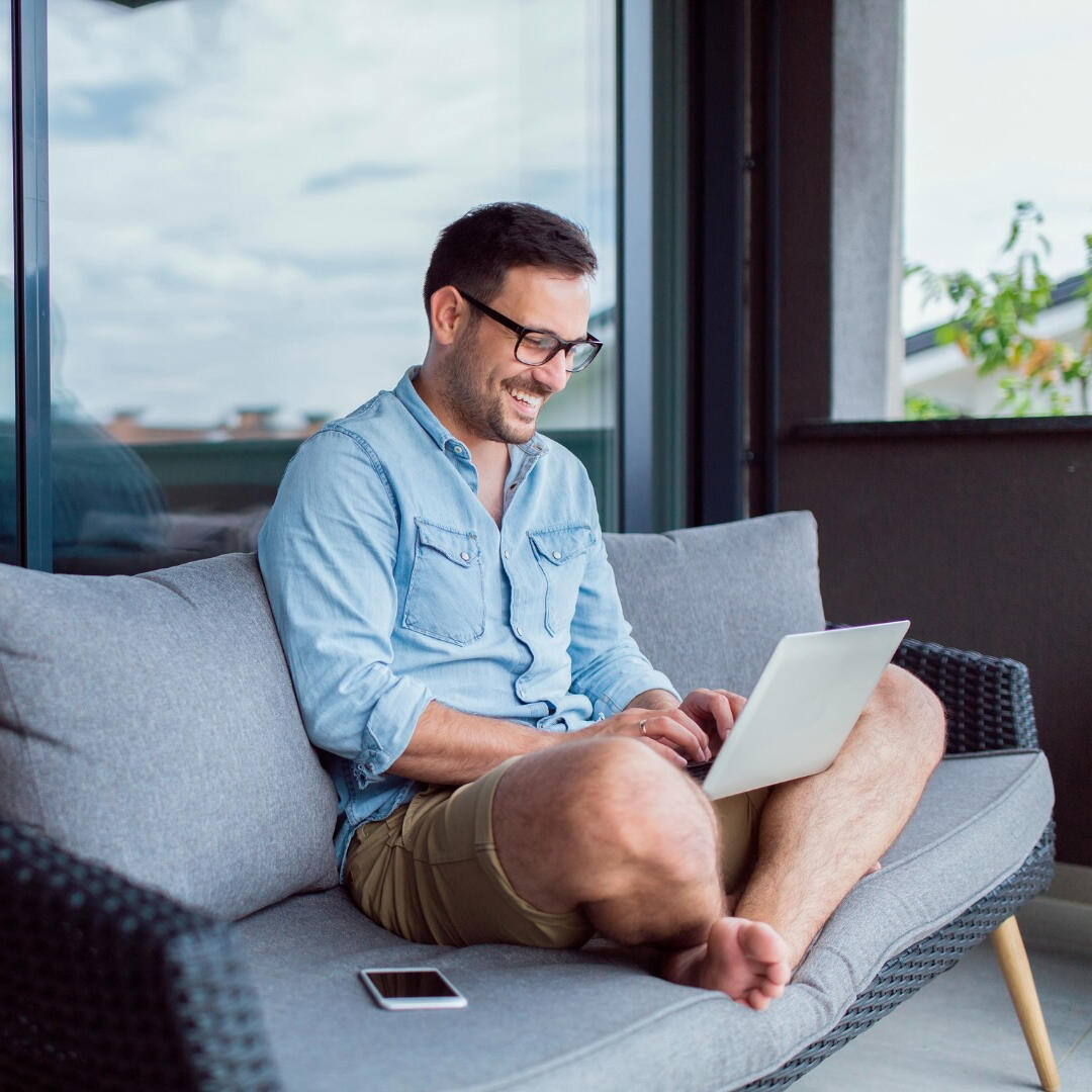 WFG Beteiligung (Digital-) Hotellerie Mann lacht und arbeitet am Laptop auf Couch